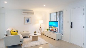 A modern living room with a sofa, a coffee table, a TV, and a lamp. - 4BR Luxury Retreat (Gold Coast)