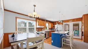 A modern kitchen with wooden cabinets, a central island, and a dining area with chairs. - 3BR Duck cottage in Sound Sea, near the beach and Duck village. (Duck)