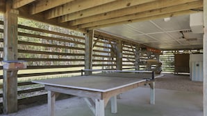 A ping pong table under a wooden structure with a roof, surrounded by wooden slats and a concrete floor. - 3BR Duck cottage in Sound Sea, near the beach and Duck village. (Duck)