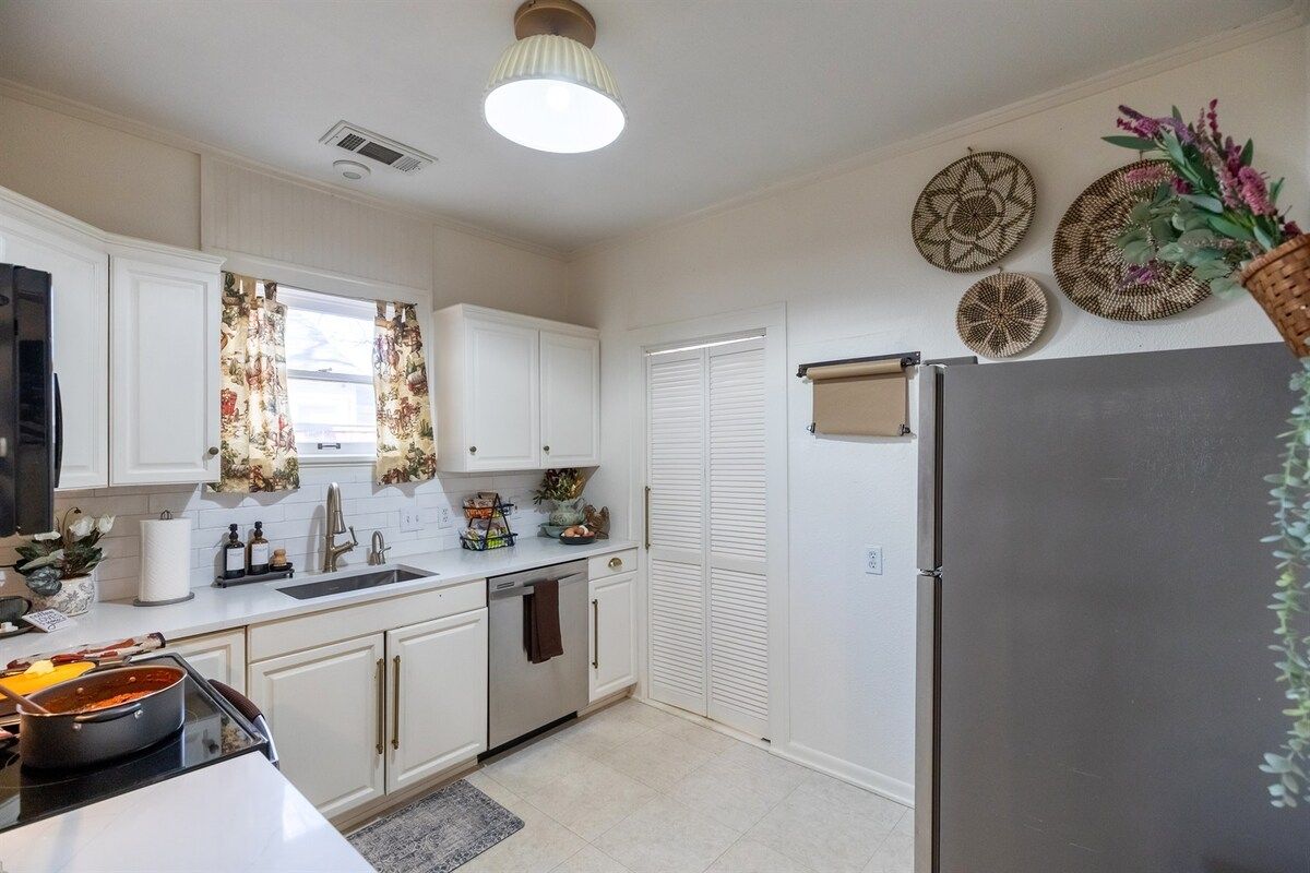 A kitchen with white cabinets, a stainless steel refrigerator, and decorative woven wall hangings.