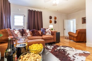 A living room with a sofa, a coffee table with snacks, a bottle, and a glass. - Cowboys and Fairytales Movie Theater  Games (Abilene)
