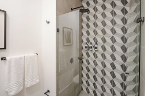 A modern bathroom with a glass shower enclosure, geometric patterned tiles, and two white towels hanging on a rack. - Luxury boutique suite 5 stars plus free parking (Bogotá, D.C.)