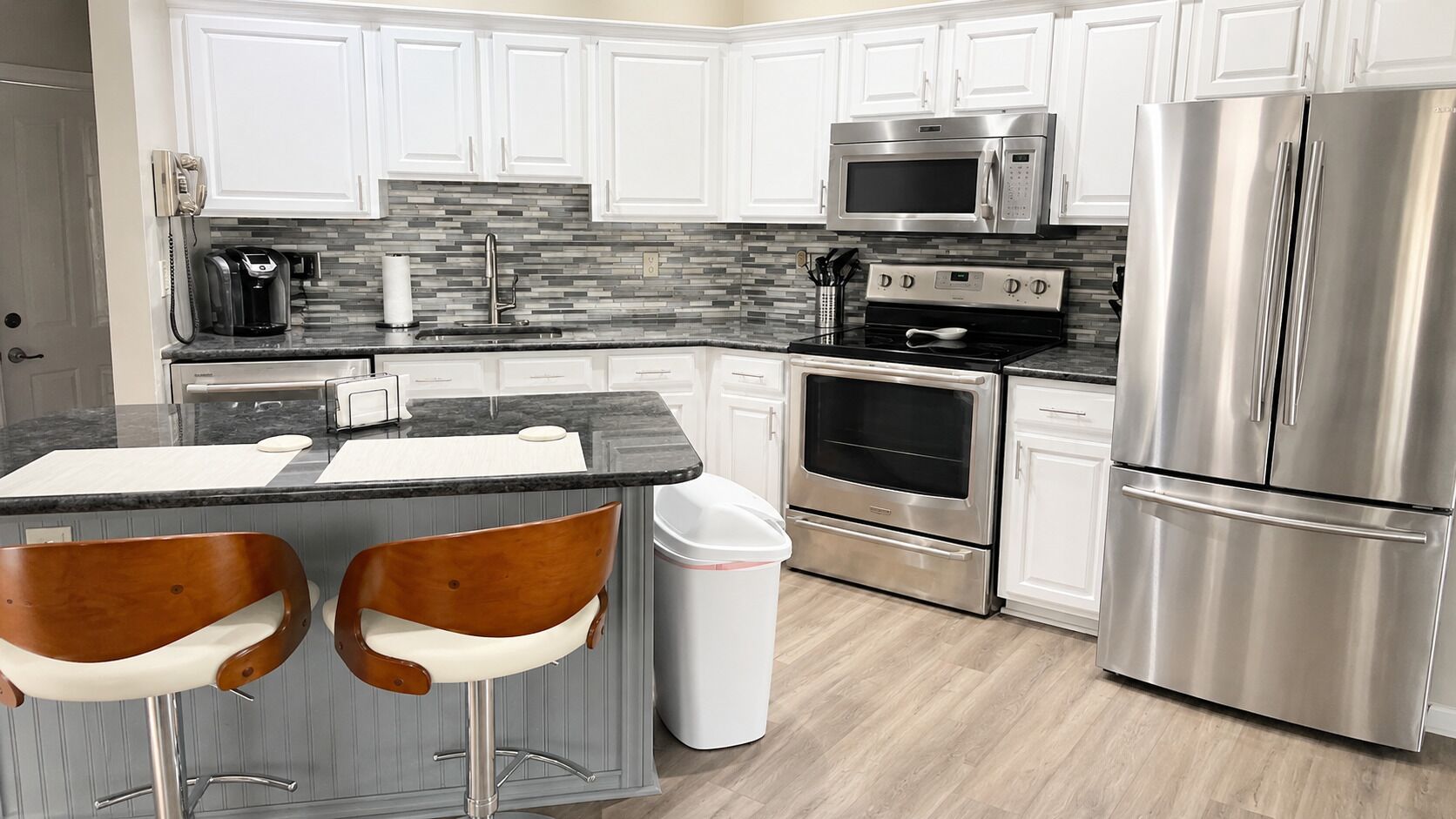A modern kitchen with white cabinets, a stainless steel refrigerator, a microwave, an oven, and a coffee maker.