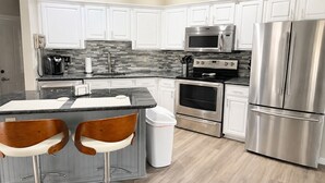A modern kitchen with white cabinets, a stainless steel refrigerator, a microwave, an oven, and a coffee maker. - Right Direction Rentals 1 Bedroom Villa 9887 (Port St. Lucie)