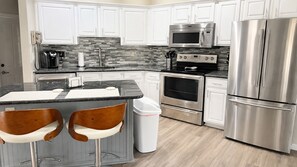 A modern kitchen with white cabinets, a stainless steel refrigerator, a microwave, an oven, and a coffee maker.