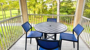 A covered outdoor patio with a round table and four chairs, surrounded by a metal railing.