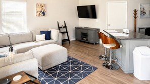 Un salon moderne avec un canapé, un pouf et un coin bar équipé de tabourets.