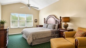 Een slaapkamer met een bed, een stoel, een nachtkastje, een lamp, een plafondventilator en een raam met jaloezieën.