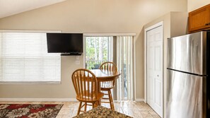A kitchen with a dining table, chairs, a TV, a refrigerator, and a sliding glass door to the outside. - Right Direction Rentals 2 Bedroom Villa 9897 (Port St. Lucie)