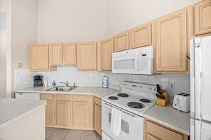 A modern kitchen with wooden cabinets, a built-in microwave, a stove, and a refrigerator. - Right Direction Rentals 2 Bedroom Villa 9906 (Port St. Lucie)
