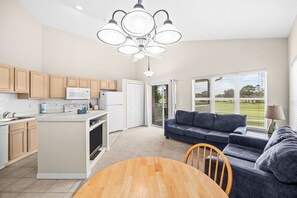 A modern kitchen with a central island, a dining area with a wooden table, and a living room with a sofa. - Right Direction Rentals 2 Bedroom Villa 9906 (Port St. Lucie)