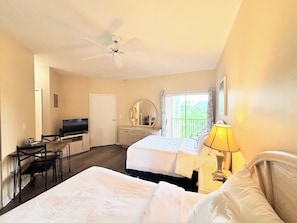 Ein Hotelzimmer mit zwei Betten, einem Schreibtisch mit Fernseher, einem Schminktisch und einem Balkon mit Blick.