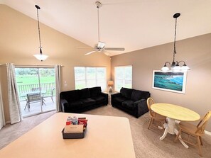 Ein Zimmer mit Deckenventilator, Tisch mit Stühlen, einer schwarzen Couch und einem Fenster mit Jalousien.