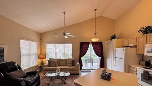 Ein Wohnzimmer mit einer Couch, einem Couchtisch, einem Essbereich mit Küchenzeile und einem Deckenventilator.