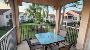 Ein Balkon mit Glastisch und Stühlen, der auf einen Innenhof mit Palmen und Wohnhäusern blickt.