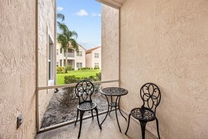 A balcony with two chairs and a small table, overlooking a building with a green lawn and a clear sky. - Right Direction Rentals 2 Bedroom Villa 9955 (Port St. Lucie)