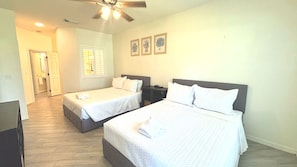 Une chambre d’hôtel avec deux lits, un ventilateur de plafond, une fenêtre avec des stores et une porte donnant sur une autre pièce.