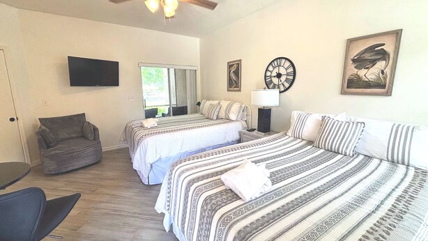 A room with two beds, a sofa, a chair, a flat-screen TV, a clock, and a framed picture on the wall. - Right Direction Rentals Studio Villa 9970 (Port St. Lucie)