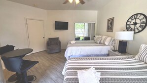 A bedroom with two beds, a TV, a ceiling fan, a chair, and a table. - Right Direction Rentals Studio Villa 9970 (Port St. Lucie)