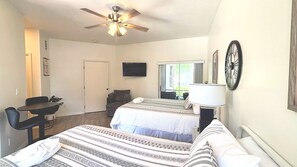 Une chambre d’hôtel avec deux lits, un bureau, une chaise, une télévision, un ventilateur de plafond et une fenêtre.