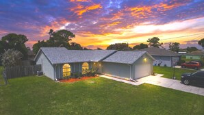 A residential house with a two-car garage, a fenced yard, and a driveway. - Right Direction Rentals Owl's Oasis (Port St Lucie)