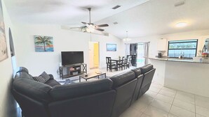 A living room with a sofa, TV, ceiling fan, and artwork on the walls. - Right Direction Rentals Owl's Oasis (Port St Lucie)