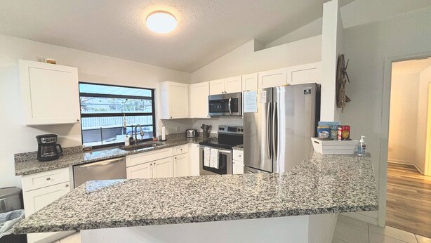 A modern kitchen with white cabinets, granite countertops, stainless steel appliances, and a window with a view. - Right Direction Rentals Owl's Oasis (Port St Lucie)