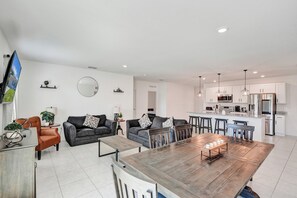 Een moderne woonkamer met een eettafel, banken en een keuken met witte kasten en roestvrijstalen apparatuur.