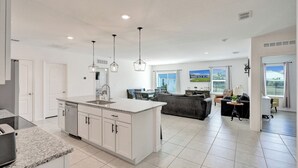 Une cuisine moderne avec des meubles blancs, des plans de travail en granit et des luminaires suspendus.