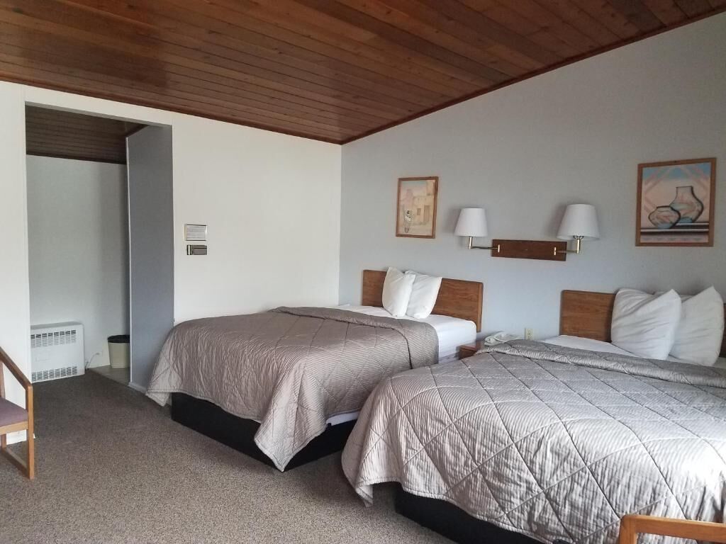 A bedroom with two beds, a wooden ceiling, and a small table.