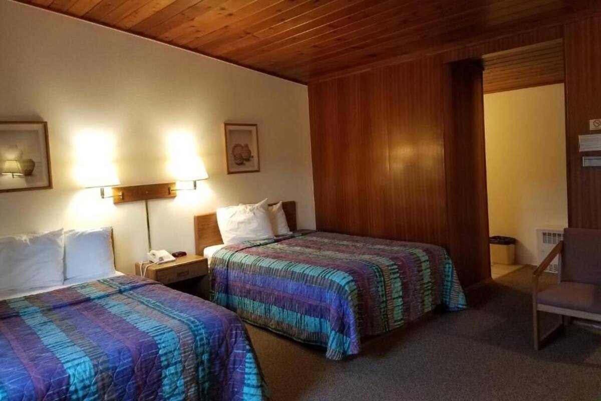 A hotel room with two beds, wooden ceiling, and a chair.