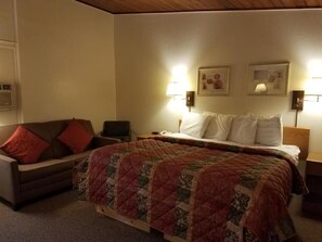 Ein Schlafzimmer mit einem Bett, einem Sessel, einer Couch, zwei Wandleuchten und einem gerahmten Bild an der Wand.