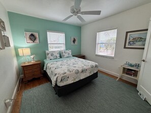 A bedroom with a bed, two bedside tables, a ceiling fan, and two windows with blinds.