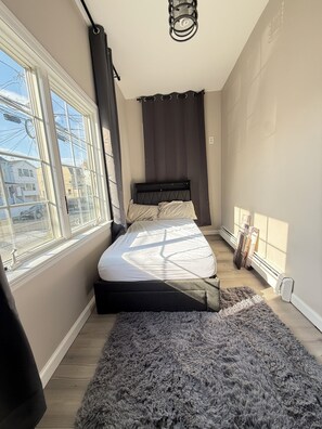 Une chambre à coucher avec un lit, une fenêtre, un radiateur et un luminaire au plafond.