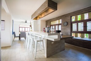 A modern kitchen with a central island, bar stools, a clock, and large windows. - Nice house in hotel zone (Cancún)