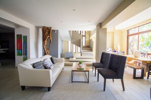 A modern living room with a sofa, armchair, coffee table, and a staircase leading to another level. - Nice house in hotel zone (Cancún)