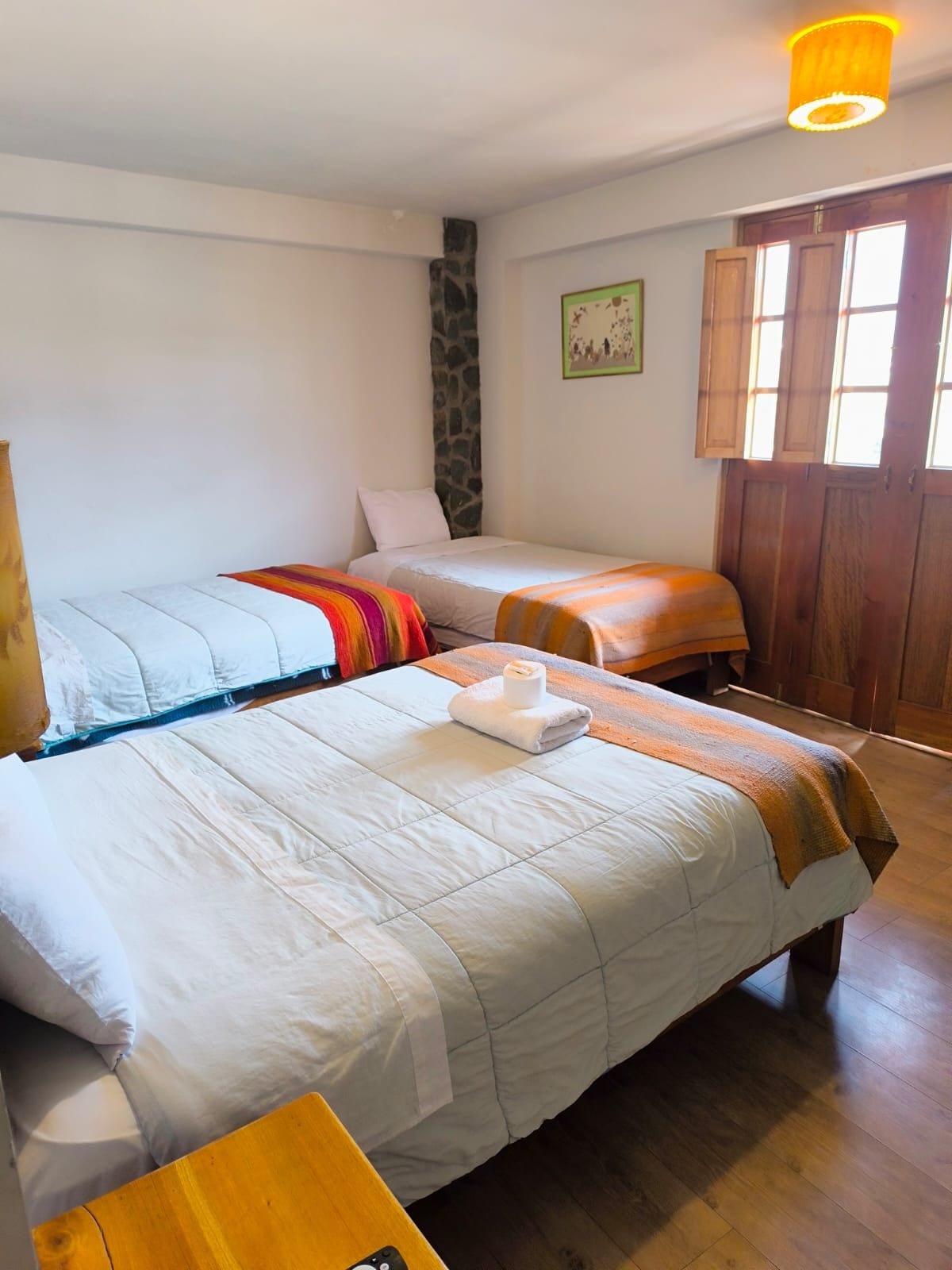Quarto com duas camas, parede de pedra, porta de madeira e uma janela.