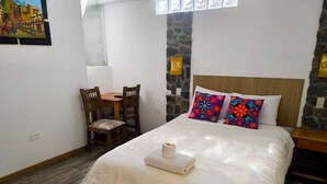 Une chambre à coucher avec un lit, une petite table, des chaises, un mur en pierre et une fenêtre.
