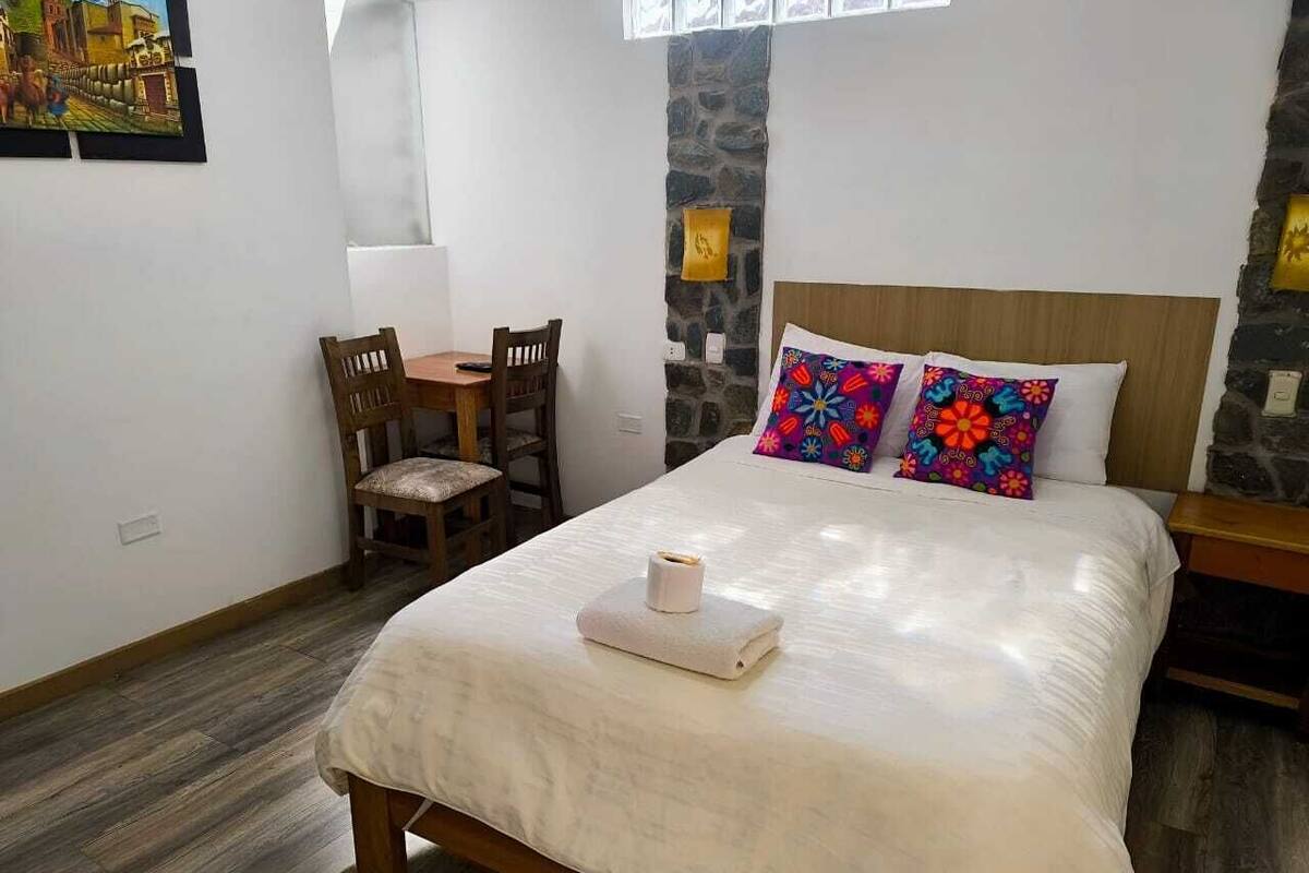 A bedroom with a bed, a small table, chairs, a stone wall, and a window.