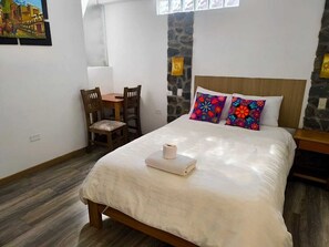 A bedroom with a bed, a small table, chairs, a stone wall, and a window. - Balcon de Piedra (Urubamba)