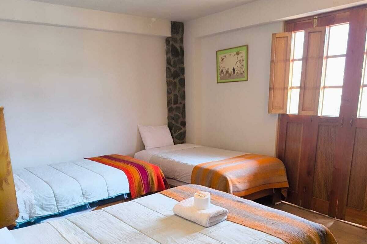 A room with two beds, a stone wall, a wooden door, and a window.