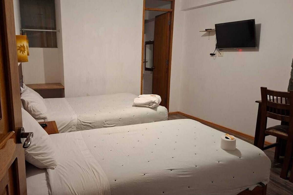 A room with two beds, a TV mounted on the wall, and a wooden chair.