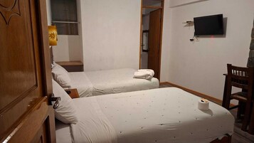 Ein Zimmer mit zwei Betten, einem an der Wand befestigten Fernseher und einem Holzstuhl.