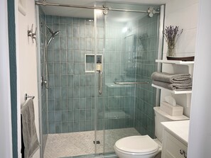 A glass-enclosed shower with a handheld showerhead, a glass door, and a tiled wall. - Saltbox by the Bay | Views, Bikes, Vetta Spa (Waubaushene)