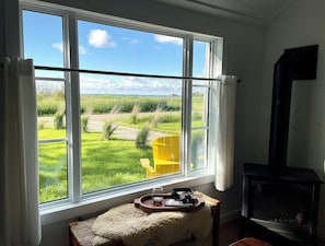 A room with a large window, a wooden bench, a small table with a tray, and a fireplace. - Saltbox by the Bay | Views, Bikes, Vetta Spa (Waubaushene)