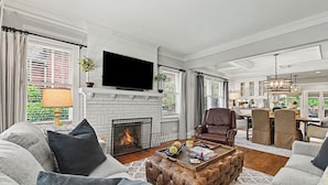 A living room with a fireplace, leather armchair, sofa, and a dining area with chairs and a table. - East Atlanta Retreat - Office + Backyard Oasis (Atlanta)