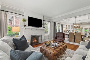 A living room with a fireplace, leather armchair, sofa, and a dining area with chairs and a table. - East Atlanta Retreat - Office + Backyard Oasis (Atlanta)