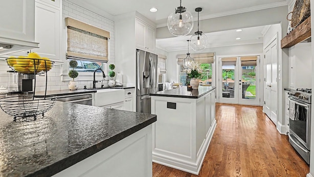 A kitchen with white cabinets, a black countertop, and a large island. There is a refrigerator, a sink, and a window with a view of the outdoors. - East Atlanta Retreat - Office + Backyard Oasis (Atlanta)