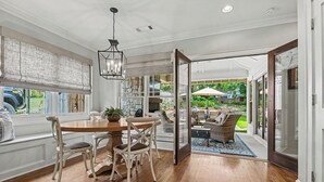 A dining area with a wooden table and chairs, a hanging light fixture, and a view of an outdoor patio with wicker furniture and a pool. - East Atlanta Retreat - Office + Backyard Oasis (Atlanta)