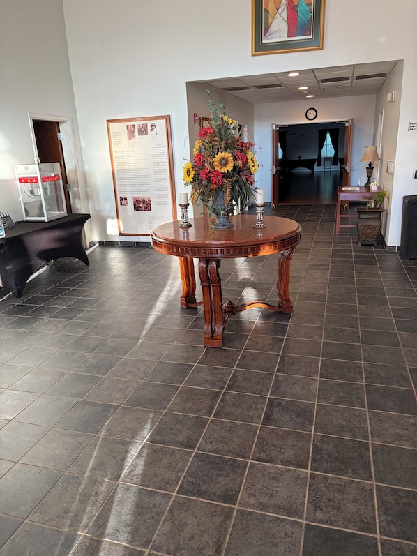 Un hall d’entrée avec une table ronde en bois, un arrangement floral, un panneau d’information encadré et une horloge au mur.